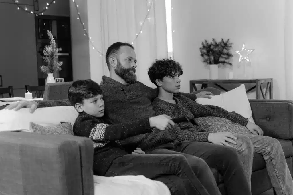 Une personne assise sur un canapé devant un écran de streaming, tenant une télécommande, dans une ambiance cosy de soiré
