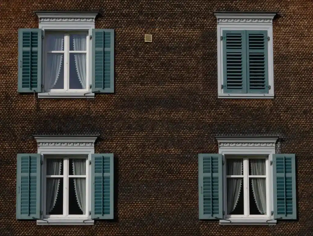 Personne en vêtements légers près d'une fenêtre avec volets fermés et ventilateur, lumière fraîche du matin