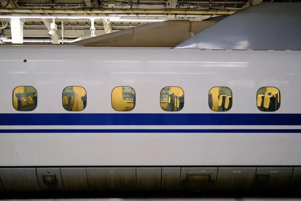 Un élève assis seul à la fenêtre d'un train, contemplant le paysage, tandis que ses camarades discutent en arrière-plan