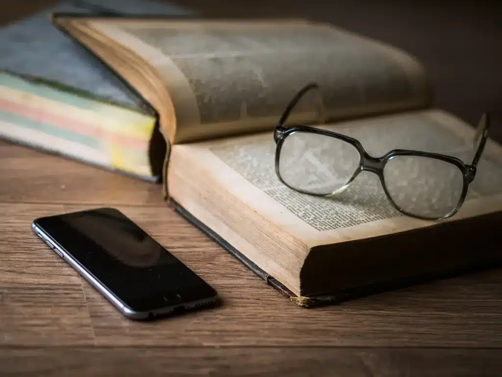 Mains feuilletant un manuscrit ancien sur une table ensoleillée avec lunettes de lecture