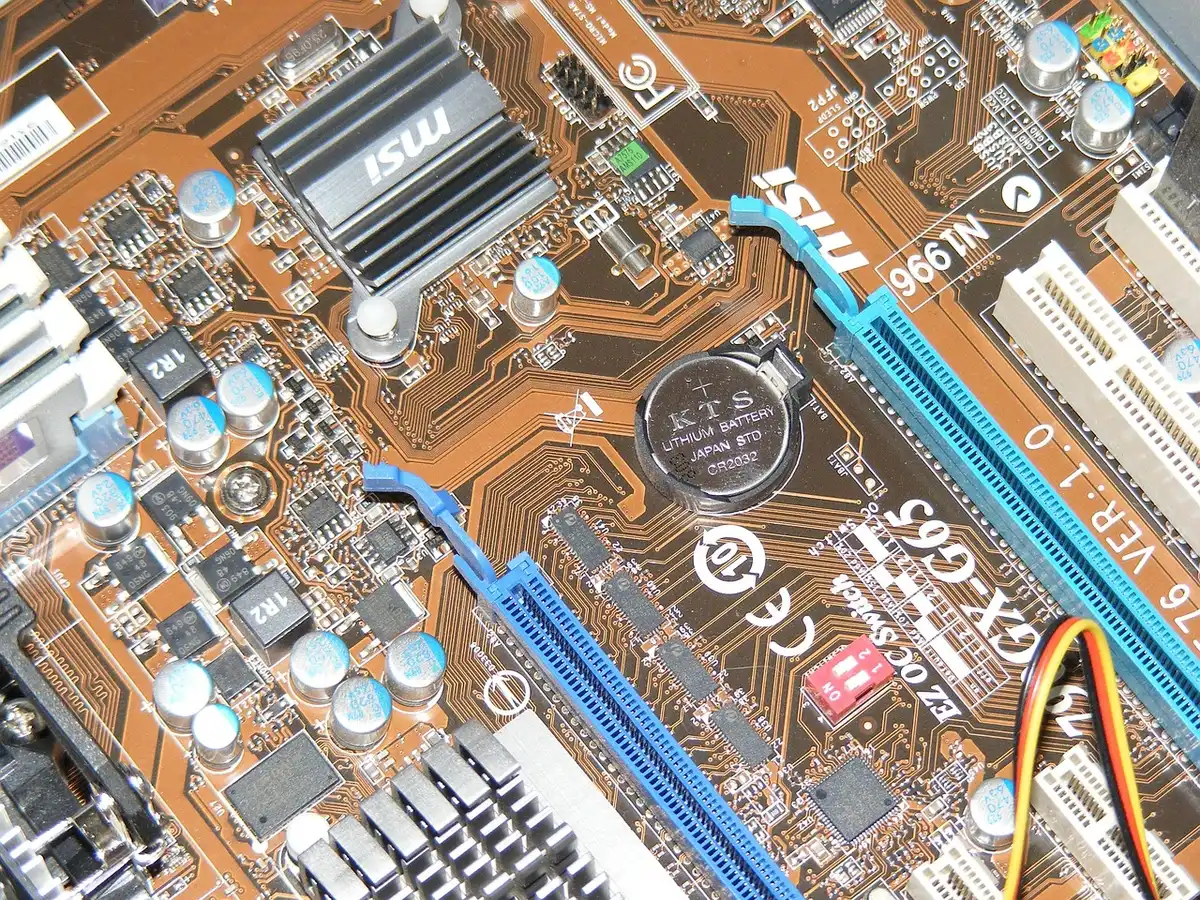 Carte mère et écran BIOS avec options visibles, pile CMOS à côté