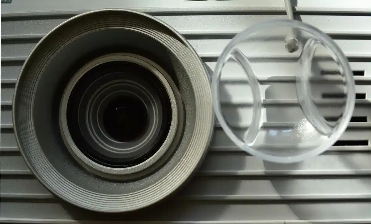 Close-up of an anonymous wireless speaker grille and projector lens on a tabletop, neutral background